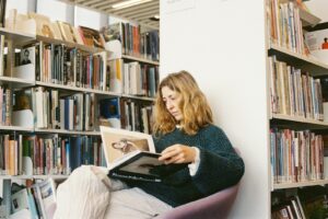 Woman reads a book surrounded by bookshelves.